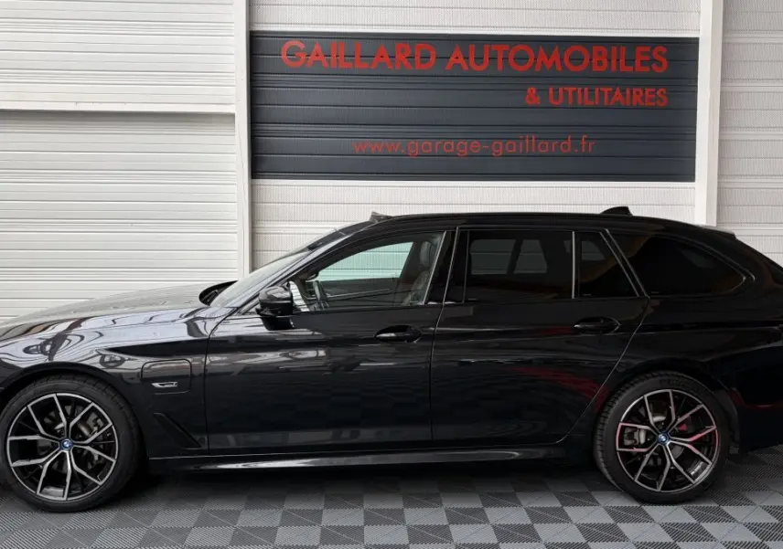 BMW Série 5 Touring 530e noir vue de profil côté gauche, avec jantes M Sport et prise de charge visible.