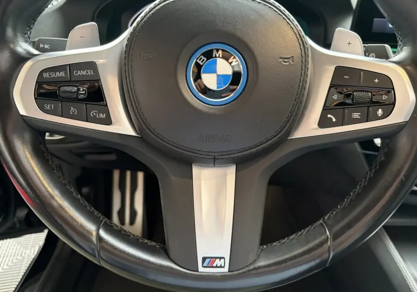Gros plan sur le volant cuir noir avec logo BMW et badge M Sport de la BMW Série 5 Touring 530e 2023.