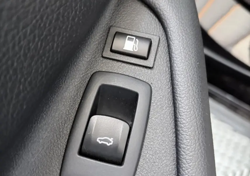 Gros plan sur les boutons d’ouverture du coffre et de la trappe à carburant dans l’habitacle noir d’une BMW Série 5 Touring 530e.