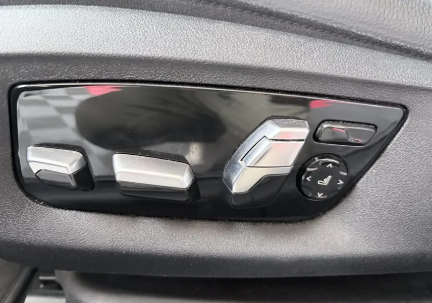Gros plan sur les commandes de réglage électrique des sièges en plastique noir et argent dans une BMW Série 5 Touring noire.