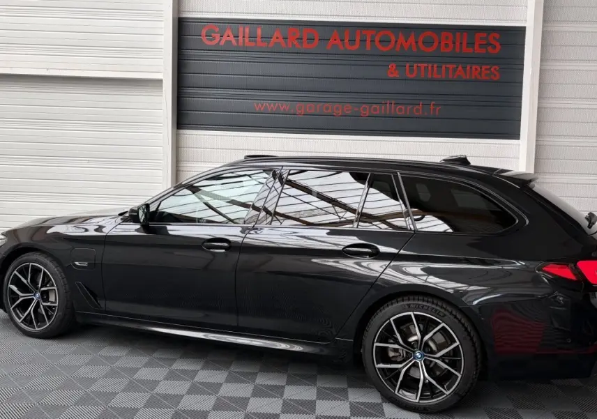 BMW Série 5 Touring 530e noire vue de profil côté gauche, avec jantes sport et vitres teintées.