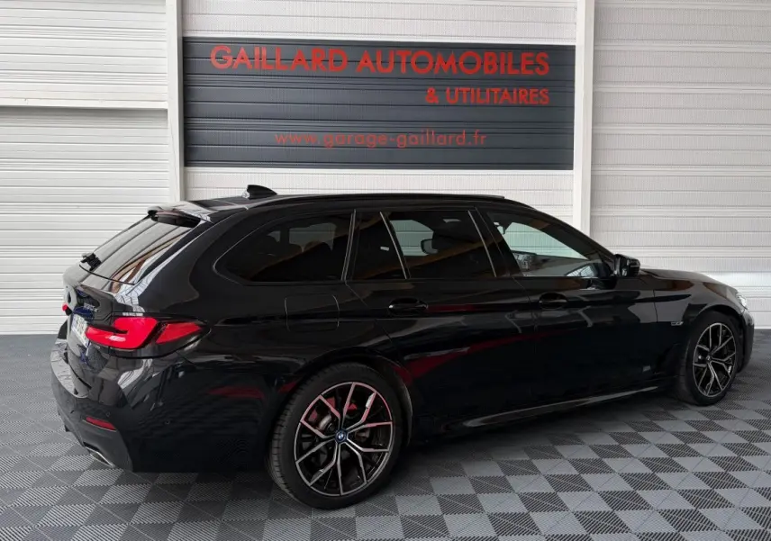 BMW Série 5 Touring 530e noire vue 3/4 arrière droit, avec jantes sport et vitres teintées.