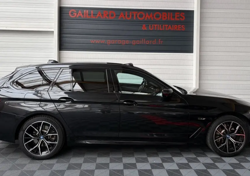 BMW Série 5 Touring 530e noire vue de profil côté gauche, avec jantes sport et vitres teintées.