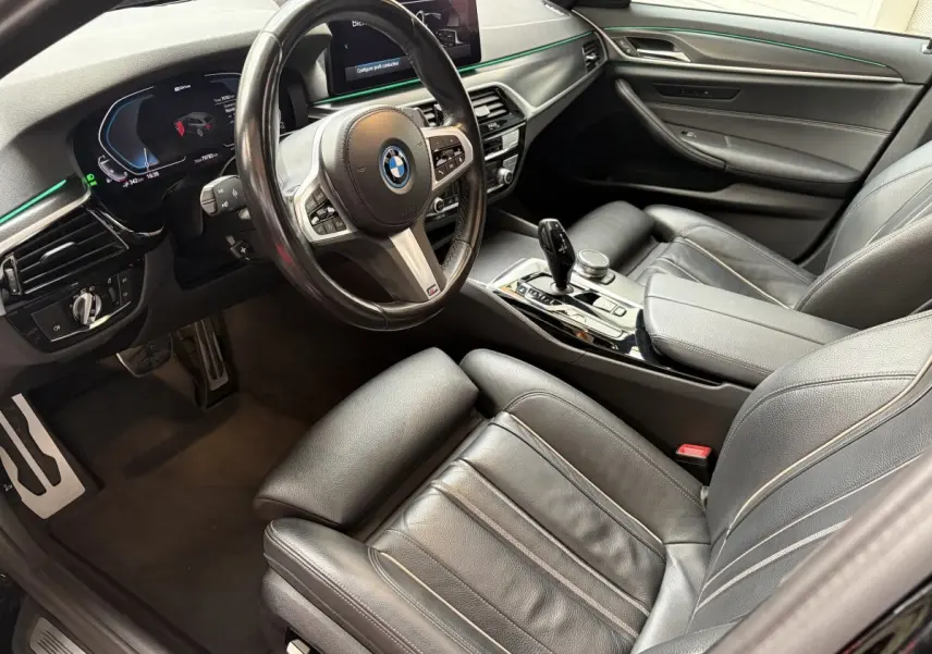Vue intérieure côté conducteur de la BMW Série 5 Touring 530e noire, avec tableau de bord digital et sellerie cuir noire.
