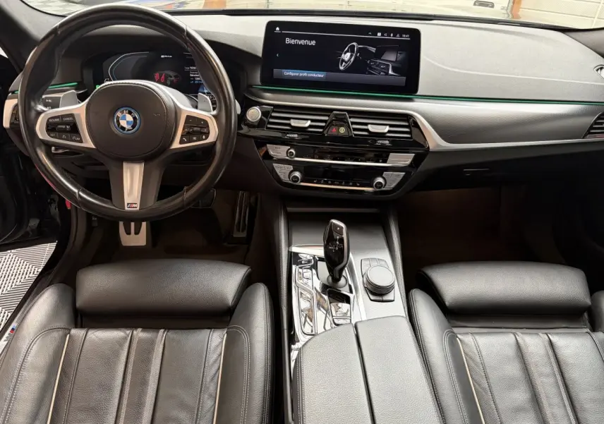 Vue intérieure avant de la BMW Série 5 Touring 530e noire, tableau de bord moderne avec écran tactile et volant M Sport.