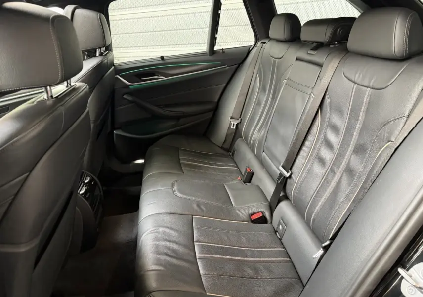 Vue intérieure arrière côté droit de la BMW Série 5 Touring 530e 2023 avec sièges cuir noirs et éclairage d'ambiance vert.