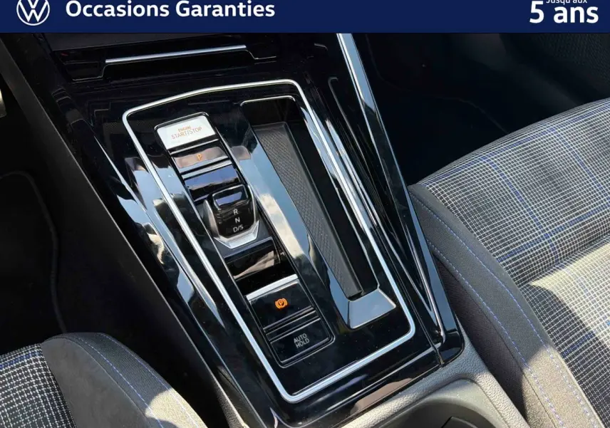 Gros plan sur la console centrale noire brillante et le siège avant à motif écossais bleu et gris de la Volkswagen Golf 1.5 eHybrid.