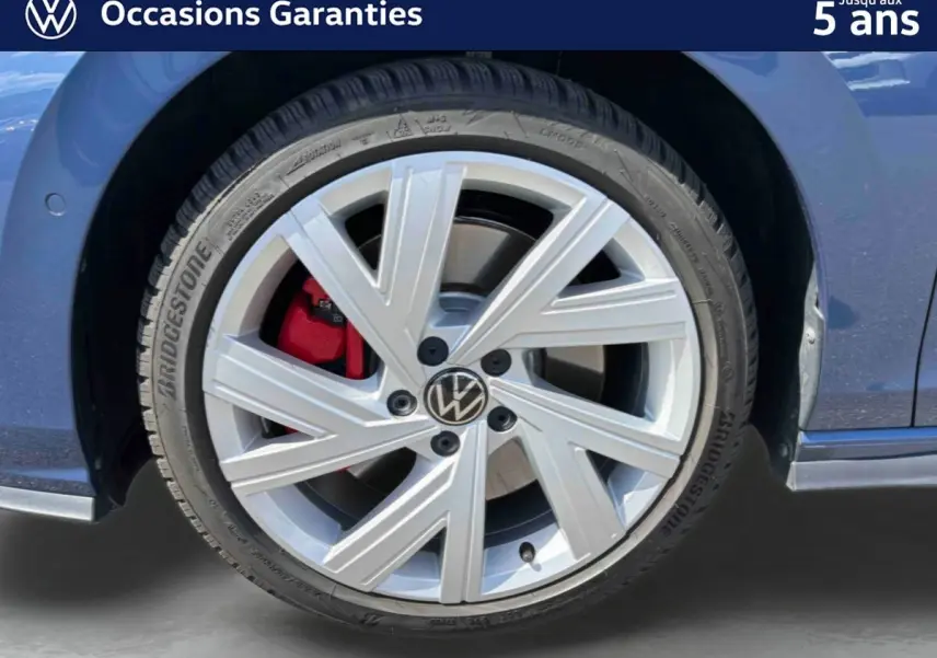Gros plan sur la roue avant gauche d'une Volkswagen Golf 1.5 eHybrid bleue avec jante alliage 17'' et étrier de frein rouge.