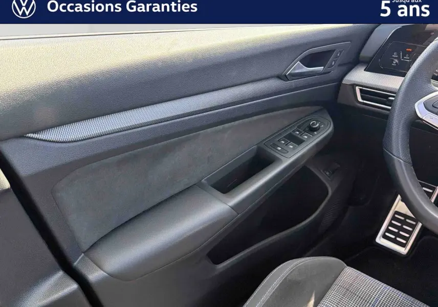 Vue intérieure côté conducteur de la Volkswagen Golf 1.5 eHybrid 2025, montrant la portière et le volant sport multifonction en cuir.