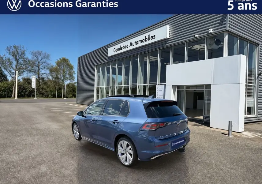 Vue 3/4 arrière droite d'une Volkswagen Golf 1.5 eHybrid 272 DSG6 bleue métallisée, avec toit panoramique et attelage rabattable.