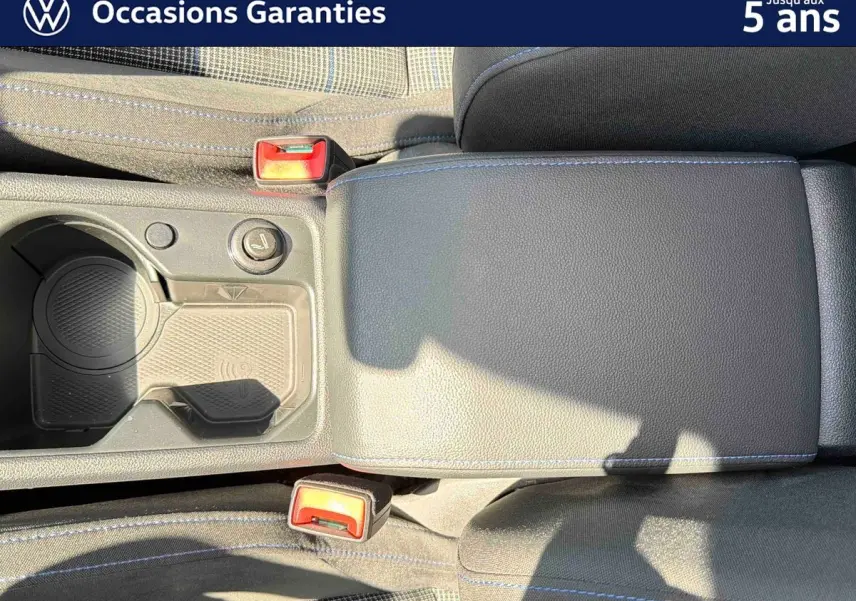 Vue rapprochée de l'accoudoir central et des porte-gobelets de la Volkswagen Golf 1.5 eHybrid 2025 en intérieur noir avec surpiqûres bleues.
