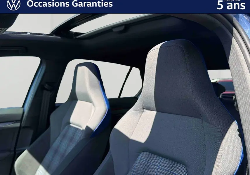 Gros plan sur les sièges sport avant gris avec surpiqûres bleues dans une Volkswagen Golf 1.5 eHybrid 2025 au toit panoramique ouvert.
