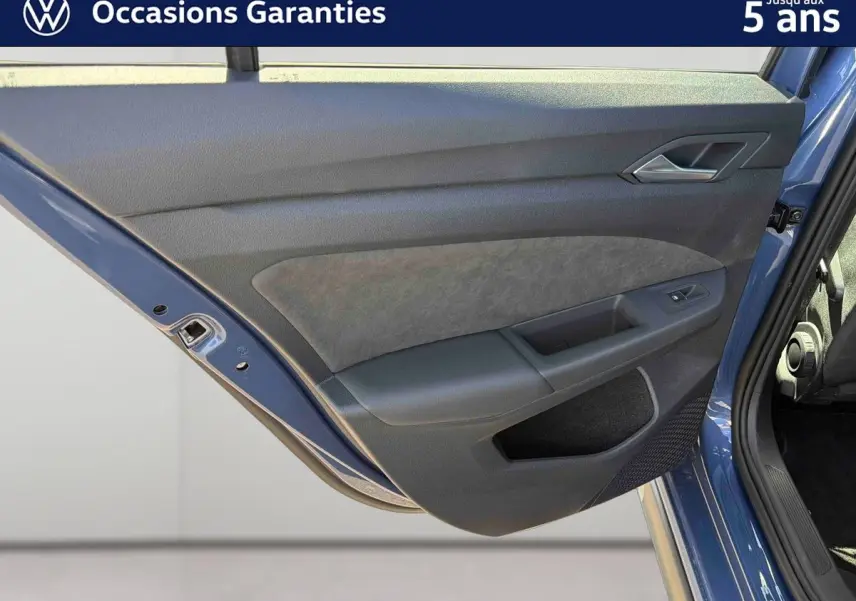 Vue rapprochée de la porte arrière gauche bleu métallisé de la Volkswagen Golf 1.5 eHybrid 2025 avec garniture intérieure grise et noire.