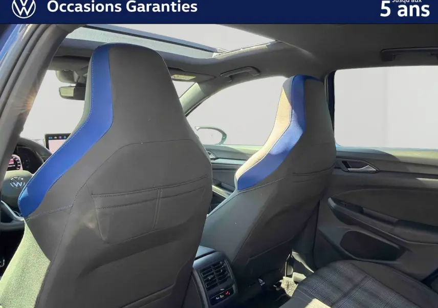 Vue intérieure arrière de la Volkswagen Golf 1.5 eHybrid 2025, sièges sport noirs avec inserts bleus et toit panoramique ouvert.