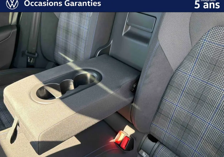 Détail de l'accoudoir central arrière avec porte-gobelets et sièges tissu à motif écossais bleu sur Volkswagen Golf 1.5 eHybrid.