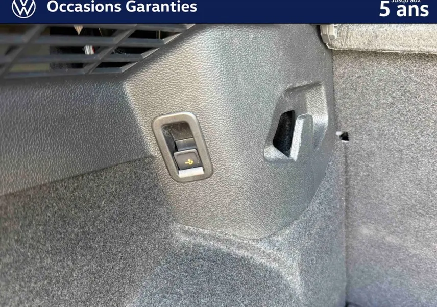 Détail intérieur du coffre de la Volkswagen Golf 1.5 eHybrid 2025, montrant un bouton de rabattement des sièges sur la paroi latérale.