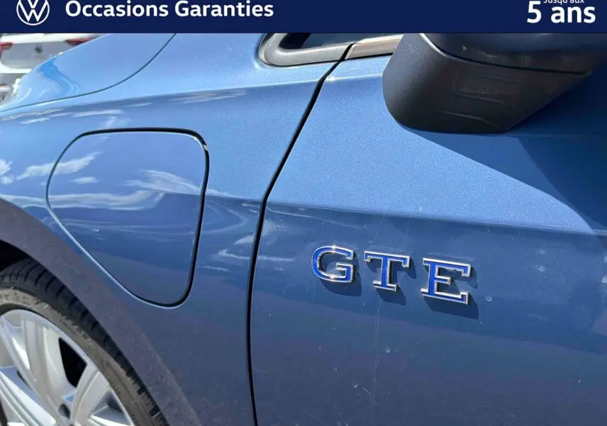 Détail côté gauche arrière d’une Volkswagen Golf 1.5 eHybrid bleue avec badge GTE et trappe de recharge visible.
