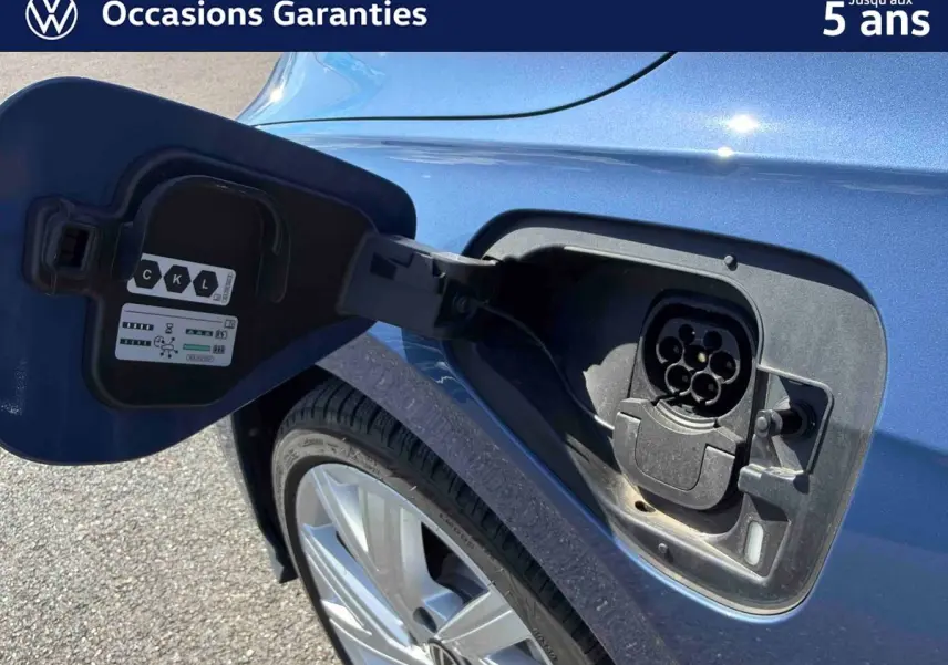 Prise de recharge ouverte côté arrière gauche sur une Volkswagen Golf 1.5 eHybrid bleue métallisée, jante alliage visible.