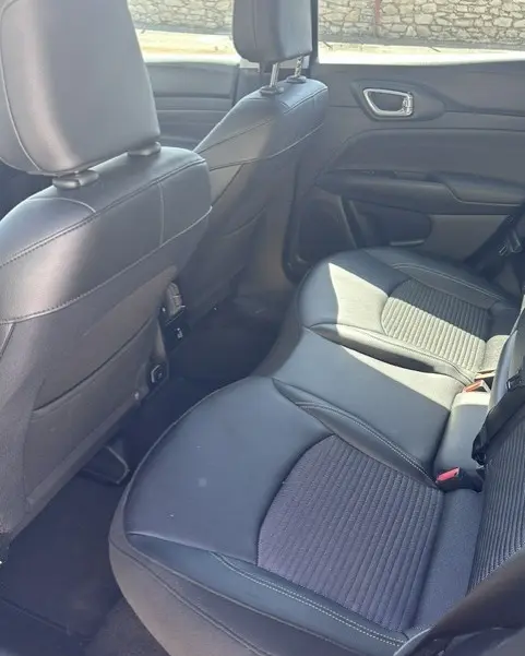 Vue intérieure arrière droite du Jeep Compass 2025 noir, montrant les sièges en cuir et tissu avec accoudoir central.