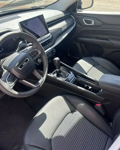 Vue intérieure côté conducteur du Jeep Compass 2025 noir, avec écran tactile central et accoudoir central visible.