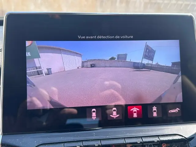 Écran tactile du Jeep Compass 2025 montrant la caméra de recul avec vue avant dégagée sur un parking extérieur.