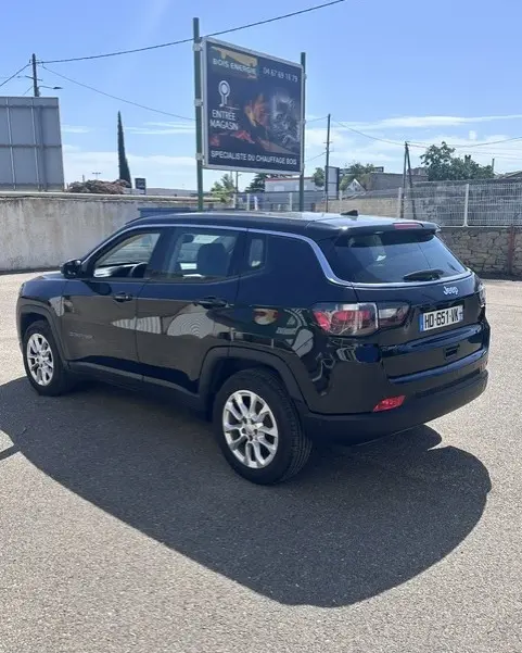 Vue 3/4 arrière droite d'un Jeep Compass noir 2025 avec jantes alliage 18 pouces, sur parking en extérieur.