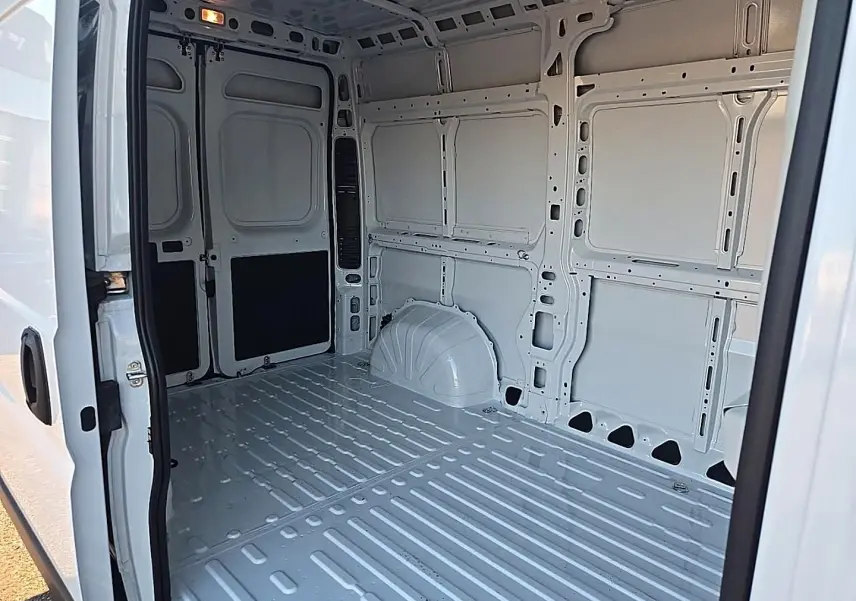 Intérieur vide du fourgon Peugeot Boxer blanc, vue en plongée depuis la porte latérale ouverte côté droit.
