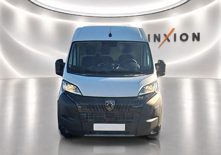 Vue de face du Peugeot Boxer Fourgon blanc 2026 avec calandre noire et phares allumés dans un studio lumineux.