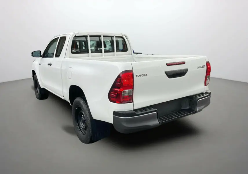 Toyota Hilux 4x4 blanc pur vu en 3/4 arrière côté gauche, avec benne ouverte et roues noires basiques.