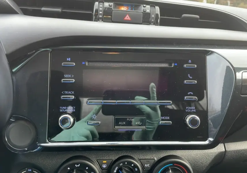 Gros plan sur la console centrale noire du Toyota Hilux 2024, avec commandes audio et climatisation visibles.