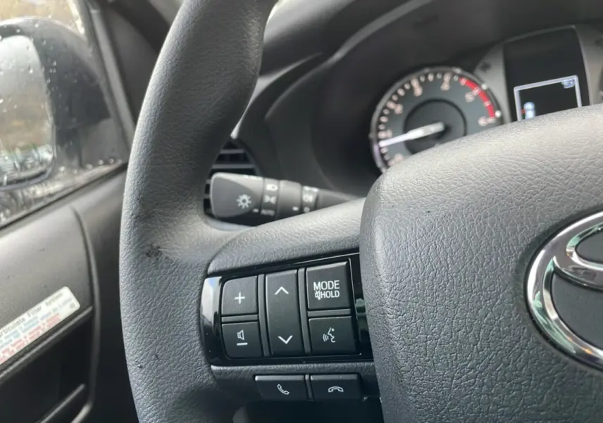 Vue rapprochée du volant noir du Toyota Hilux 2024, avec commandes multifonctions et tableau de bord partiel visible.