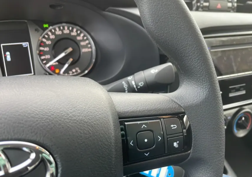Gros plan sur le volant noir du Toyota Hilux 4x4 2024 avec commandes multifonctions et tableau de bord partiel.