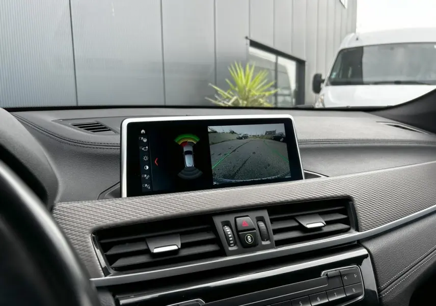 Vue du tableau de bord du BMW X2 F39 avec écran affichant la caméra de recul et les capteurs de stationnement.