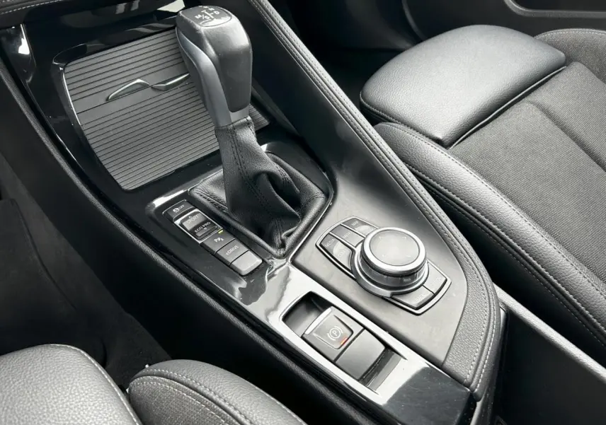 Gros plan sur la console centrale noire du BMW X2 F39 avec levier de vitesses automatique et commandes multimédia.