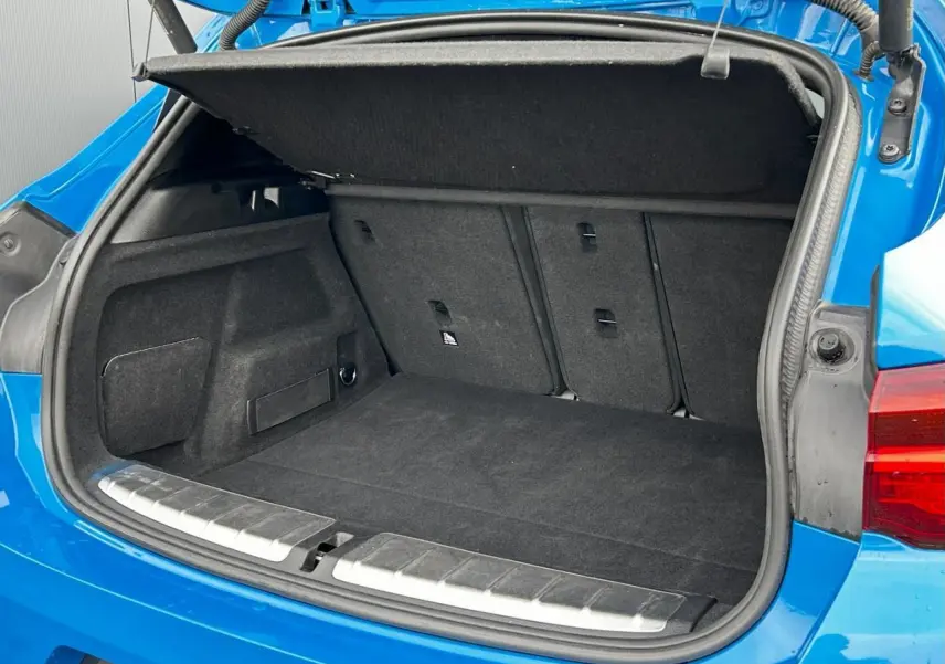 Coffre ouvert vu de l'arrière d'une BMW X2 F39 xDrive 25e bleu Misano avec hayon électrique et tapis noir.
