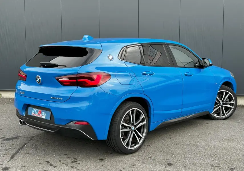 BMW X2 xDrive 25e bleu Misano vue 3/4 arrière droit avec jantes alliage bicolores et vitres teintées