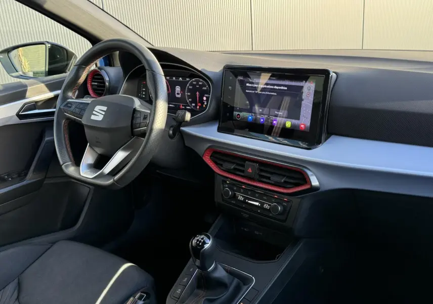Intérieur avant droit de la SEAT Ibiza TSI 115 FR 2025 avec tableau de bord noir et touches rouges, écran tactile et boîte manuelle.