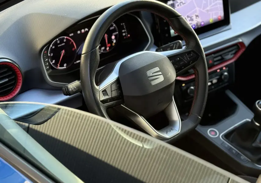 Vue rapprochée de l'intérieur de la SEAT IBIZA TSI 115 FR 2025, volant cuir avec logo SEAT et détails rouges.