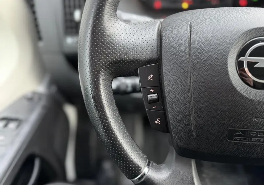 Gros plan sur le volant en cuir noir perforé de l’Opel Movano Fourgon 2024, avec commandes intégrées côté gauche.