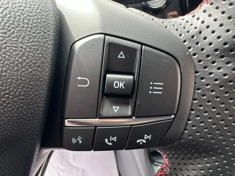 Gros plan sur les commandes multifonctions à gauche du volant perforé noir du Ford Puma 2024 finition ST-Line.