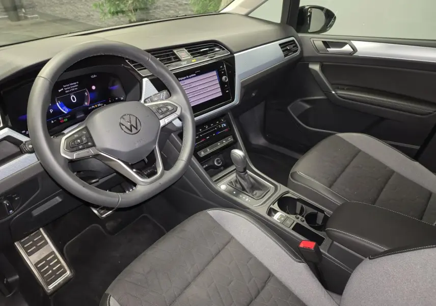 Vue intérieure côté conducteur du Volkswagen Touran 2025, montrant le volant cuir multifonction et la console centrale noire.