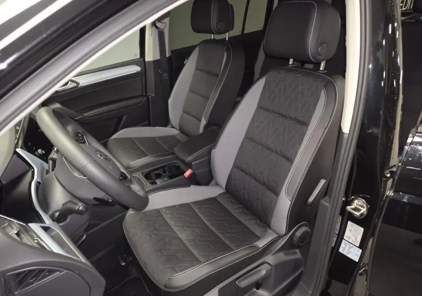 Vue intérieure côté conducteur du Volkswagen Touran noir 2025, mettant en valeur les sièges avant bi-matière gris et noir.