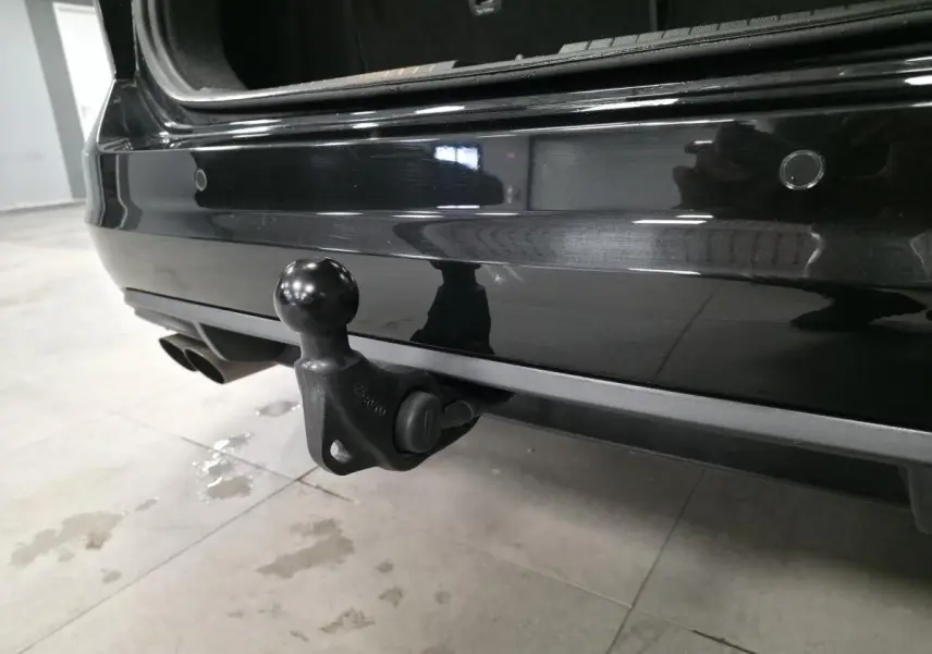 Gros plan sur l'attelage escamotable arrière du Volkswagen Touran noir, hayon ouvert, dans un garage.