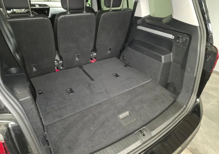 Vue arrière du coffre noir du Volkswagen Touran 2025 avec sièges rabattus et hayon ouvert montrant l'espace de chargement.