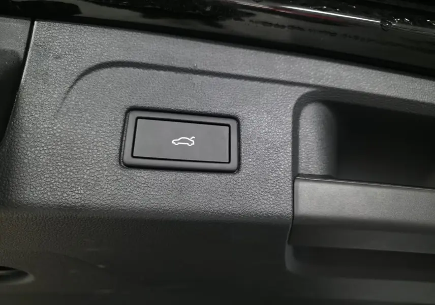 Bouton noir d'ouverture électrique du hayon sur le panneau intérieur du coffre d'un Volkswagen Touran noir.