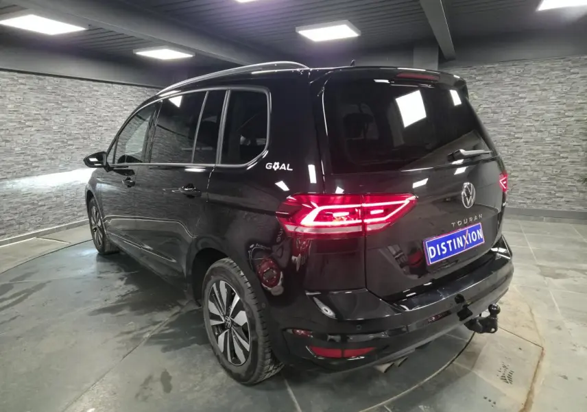 Vue 3/4 arrière droite d'un Volkswagen Touran noir intense avec hayon et crochet d'attelage escamotable visible.