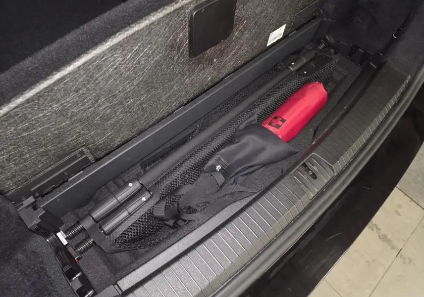 Vue en plongée sur le coffre noir du Volkswagen Touran 2025, montrant le rangement sous plancher avec accessoires.