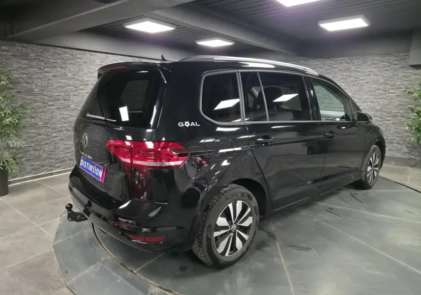 Volkswagen Touran noir 2025 en 3/4 arrière droit, hayon avec attelage escamotable et vitres surteintées.
