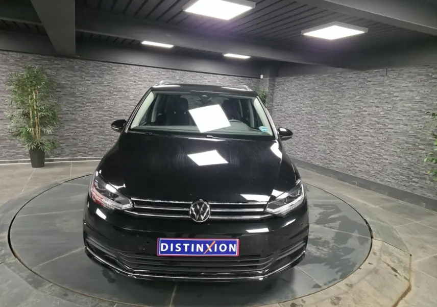 Vue avant d'un Volkswagen Touran noir nacré 2025 avec calandre chromée et plaque Distinxion en intérieur showroom.