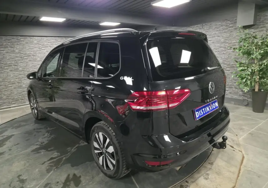 Vue 3/4 arrière droite d'un Volkswagen Touran noir avec hayon et crochet d'attelage escamotable en intérieur showroom.